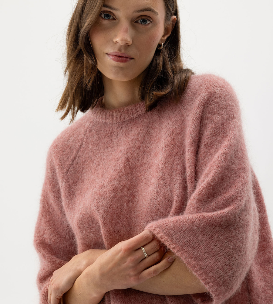 Flera stickade plagg som hänger på galge på en klädställning