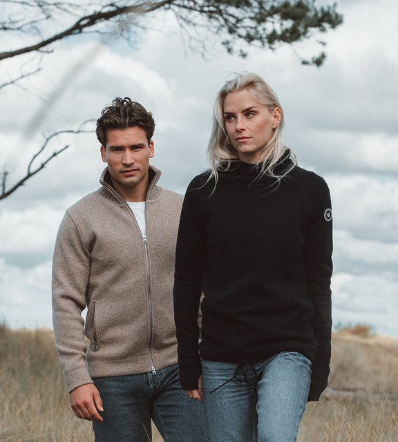 Kvinna och man går längst med strandkanten och bär linneplagg