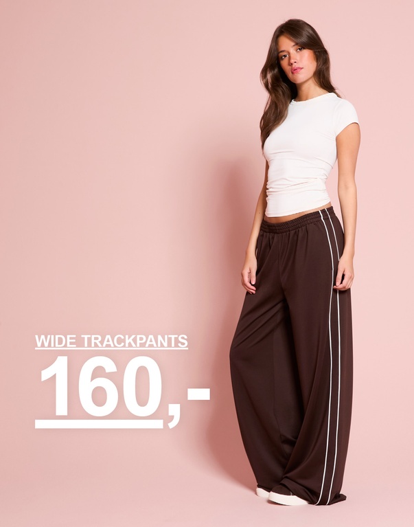 Pige har en hvid T-shirt og brune brede trackpants med hvide striber på. WIDE TRACKPANTS 20€.