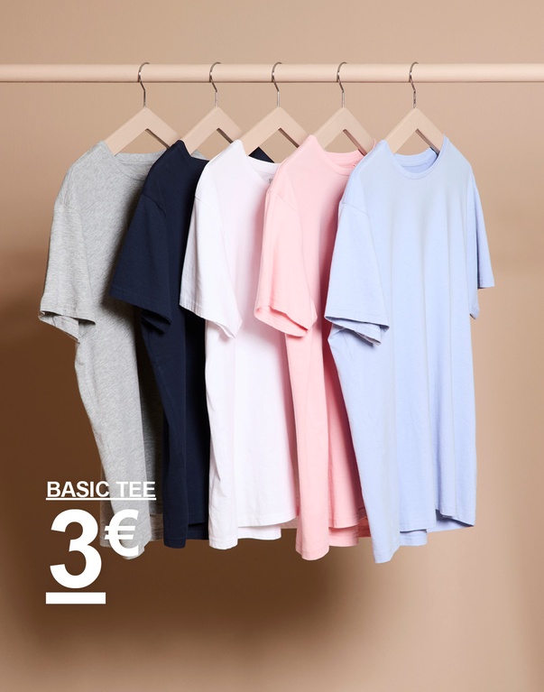 Mehrere einfarbige T-Shirts in verschiedenen Farben auf Kleiderbügeln vor hellem Hintergrund. Kampagnentext: „BASIC TEE 3€“.