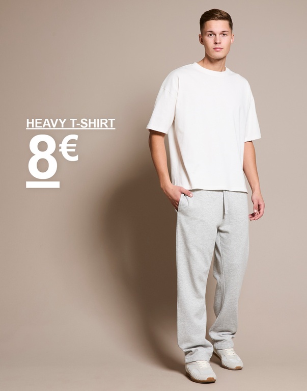 Mann in weißem T-Shirt und grauer Jogginghose steht vor beigem Hintergrund. Text auf dem Bild zeigt: „Heavy T-Shirt 8 €“.