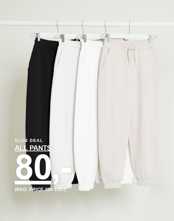 Fire joggingbukser i sort, lysegrå, hvid og beige hænger på en bøjlestang. Tekst: Club deal All pants 80,- (Reg. price 100–125,-)