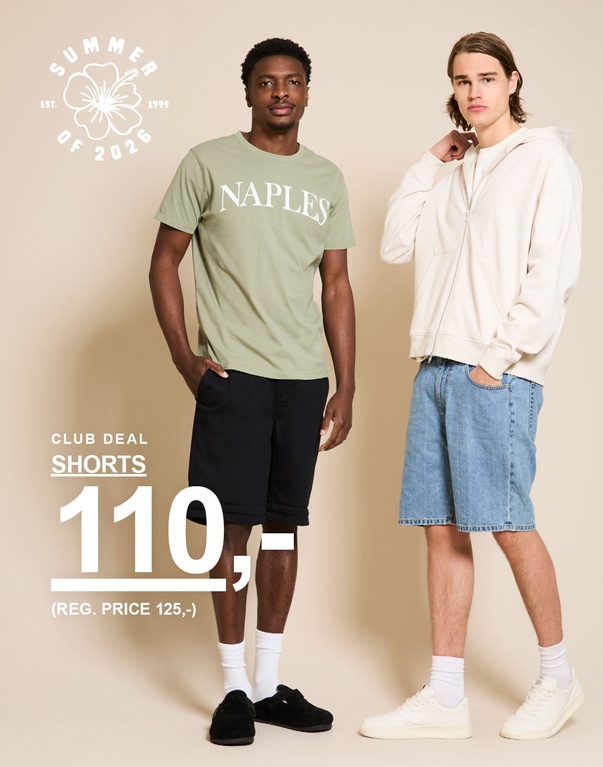 To mænd i shorts – den ene i grøn t-shirt og mørke shorts, den anden i beige hoodie og lyse denimshorts foran beige baggrund. CLUB DEAL. SHORTS 110,- (REG. PRICE 125,-)