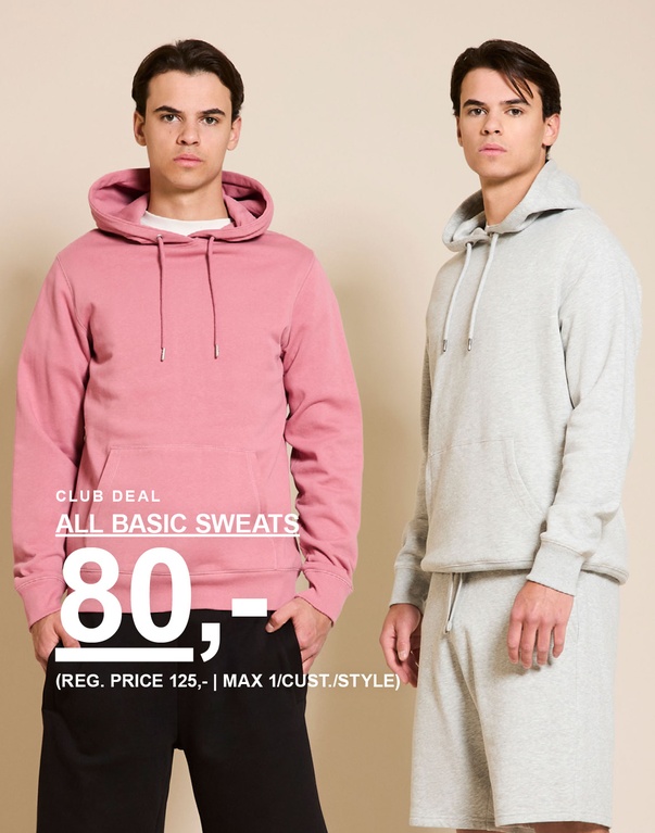 To mænd i hoodies og sweatshorts – den ene i rosa hoodie og sorte shorts, den anden i grå hoodie og matchende shorts foran en beige baggrund. CLUB DEAL. ALL BASIC SWEATS 80,- (REG. PRICE 125,- | MAX 1/CUST./STYLE)