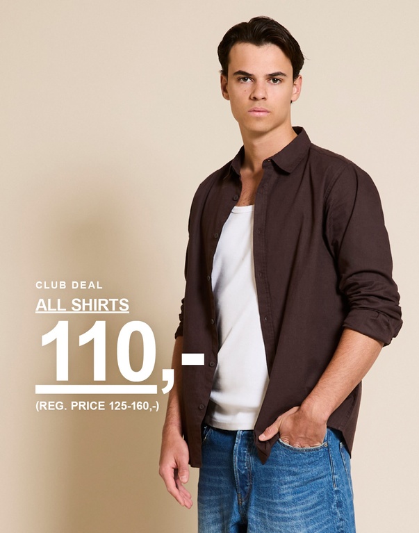 Mand i mørkebrun skjorte over en hvid top og blå denimshorts. CLUB DEAL. ALL SHIRTS 110,- (REG. PRICE 125-160,-)