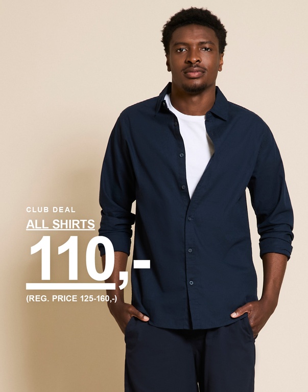 Mand i mørkebrun skjorte over en hvid top og blå denimshorts. CLUB DEAL. ALL SHIRTS 110,- (REG. PRICE 125-160,-)