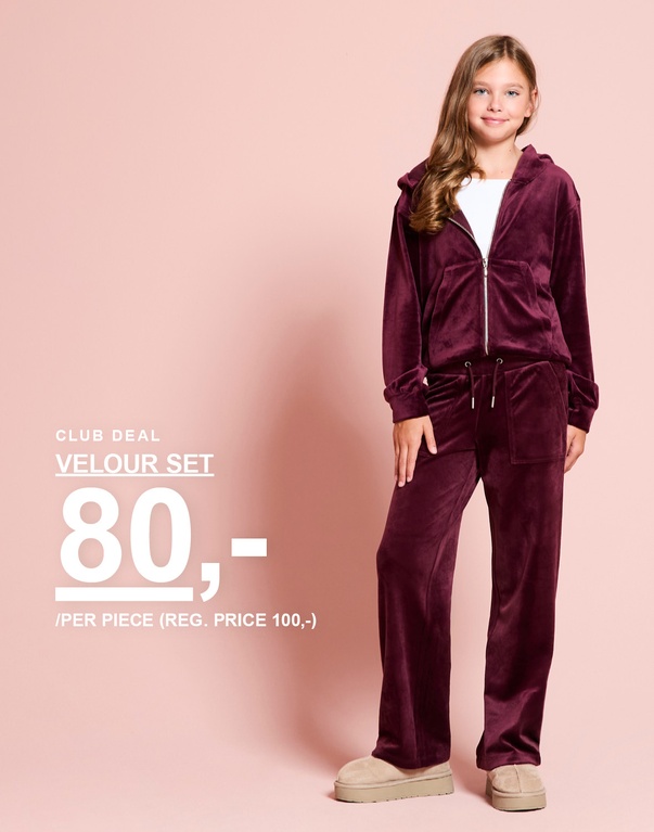 En pige har et bordeaux veloursæt på med hættetrøje og bukser. CLUB DEAL – VELOUR SET 80,- / PER PIECE (REG. PRICE 100,-).