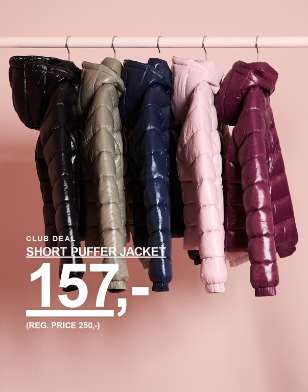 Korte pufferjakker til børn i flere farver hænger på et tøjstativ. CLUB DEAL – SHORT PUFFER JACKET 157,- (REG. PRICE 250,-).