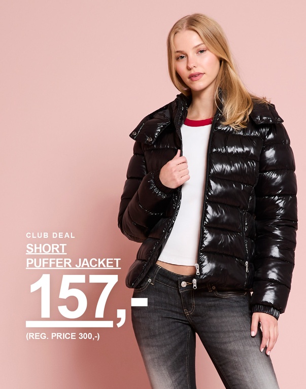 Pige i en sort, skinnende kort pufferjakke. Kampagnetekst: "CLUB DEAL – SHORT PUFFER JACKET 157,- (NORMALPRIS 300,-)".