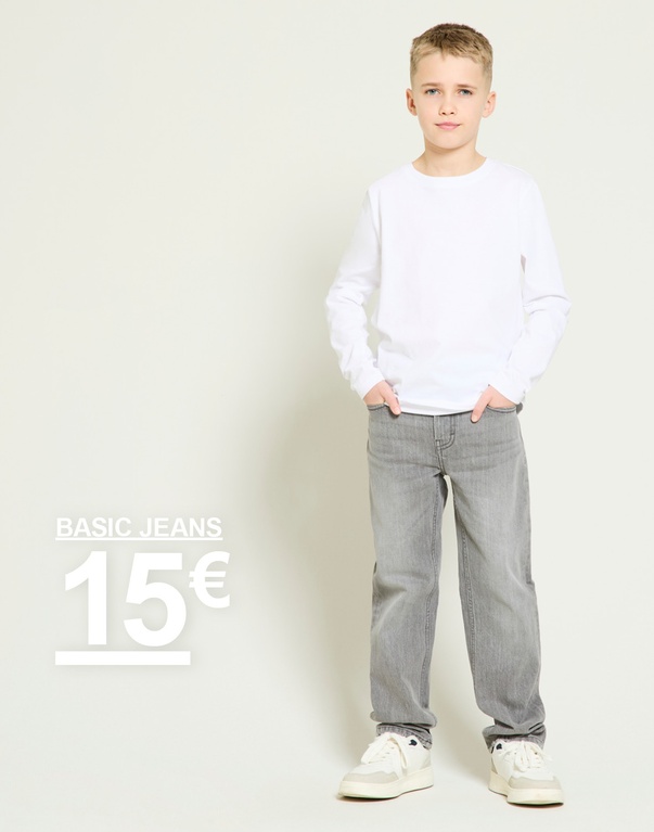 Poika valkoisessa pitkähihaisessa paidassa ja harmaissa farkuissa vaaleaa taustaa vasten. Kampanjtext: ”BASIC JEANS 15€”.