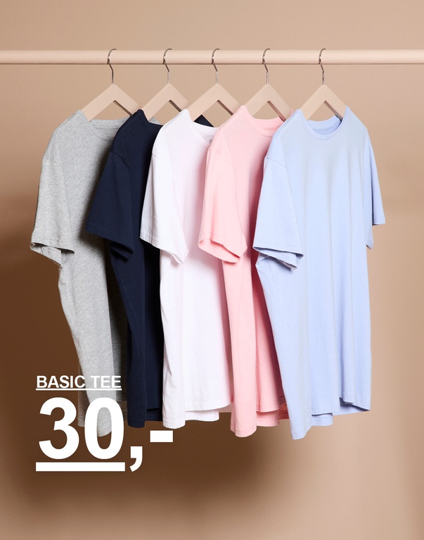 Flere ensfargede t-skjorter i ulike farger på kleshengere mot lys bakgrunn. Kampanjetekst: ”BASIC TEE 30,-”.