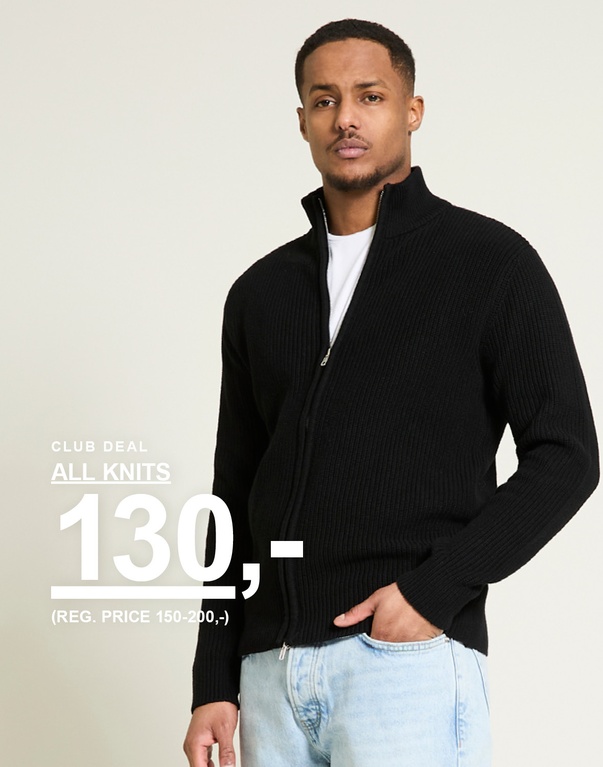 Mann i svart ribbestrikket jakke med glidelås og lyse jeans mot lys bakgrunn. Club deal all knits 130,- (reg. price 150-200,-)