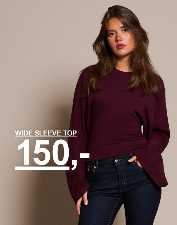 "Jente i burgunder topp med vide ermer og mørkeblå jeans. Kampanjtekst: 'WIDE SLEEVE TOP, 150,-'."