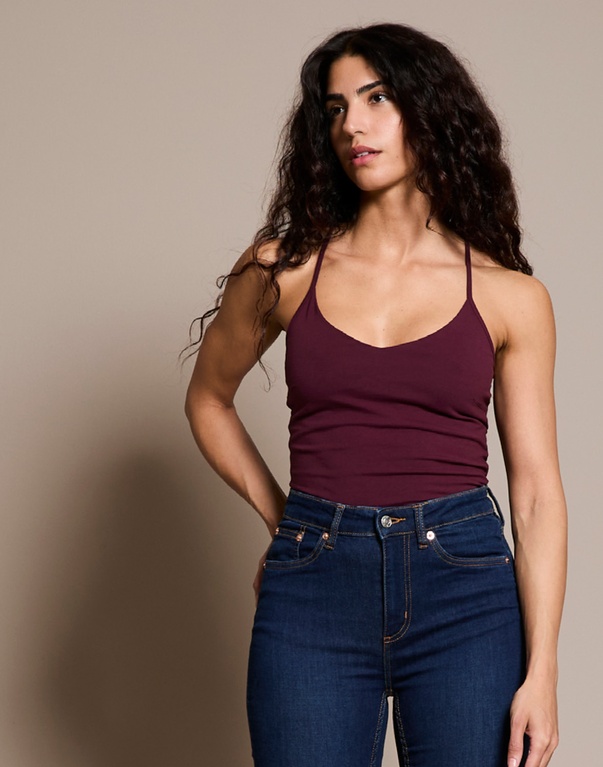 Kvinde i vinrød top og blå jeans. Tekst: "GREAT BASICS FOR ALL PEOPLE" med beskrivelse af Lager 157’s idé om prisvenlige basisvarer med gennemtænkt design og høj kvalitet.