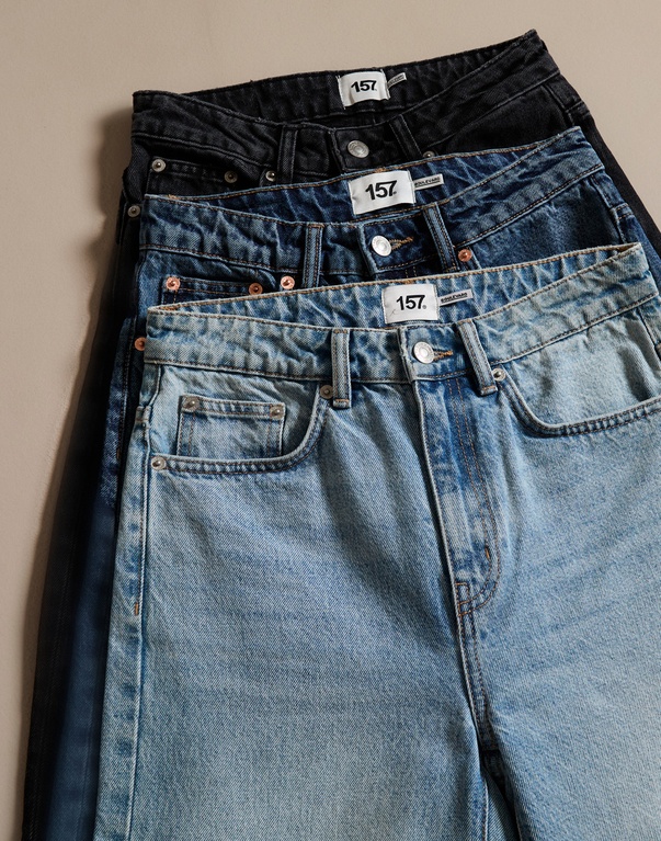 Pino taiteltuja farkkuja eri sinisen ja harmaan sävyissä. Teksti: "DENIM" ja tietoa laajasta farkkuvalikoimasta kaikille ikäryhmille ja vartalotyypeille, painottaen istuvuutta, laatua ja kestävyyttä.