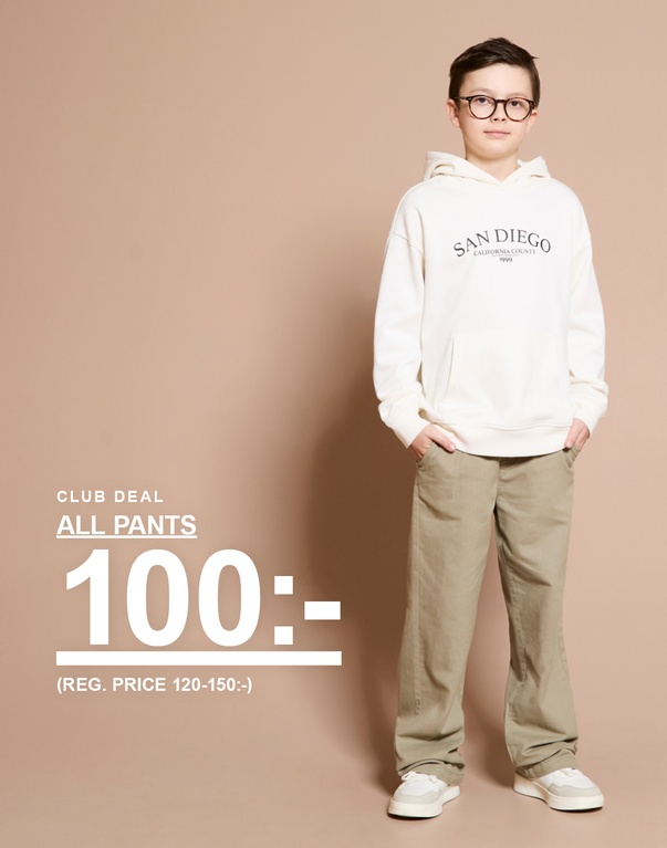 Barn i vit hoodie och beige byxor står mot ljus bakgrund. Text: ”Club deal All pants 100:- (ord. pris 120–150:-)”.