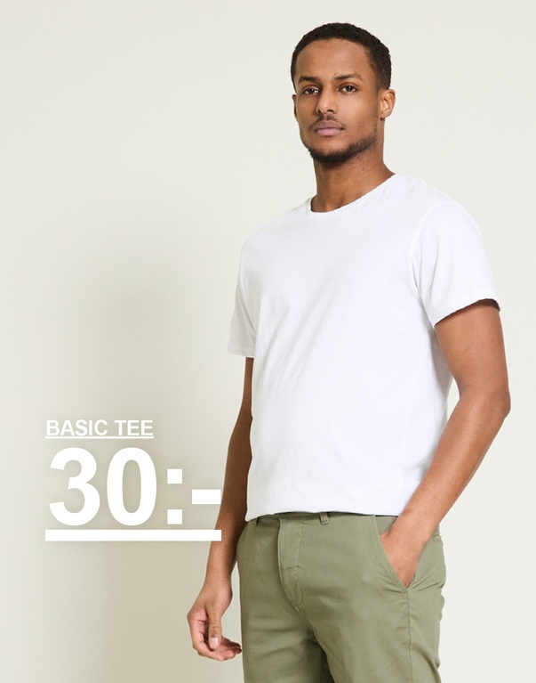 Man i vit basic t-shirt och gröna byxor mot ljus bakgrund. Basic tee 30:-