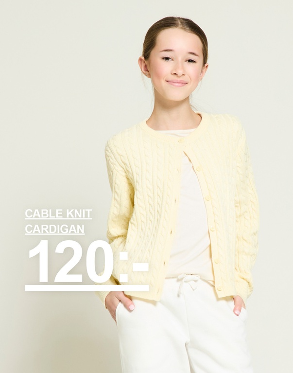 Ett barn i gul kabelstickad kofta och ljusa byxor. Kampanjtext: ”CABLE KNIT CARDIGAN, 120:-”