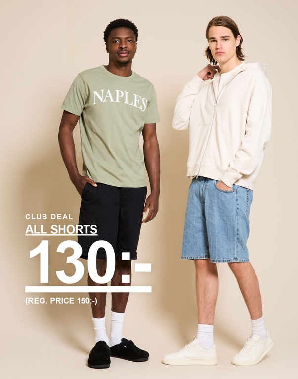 Två män i shorts – den ena i grön “NAPLES”-t-shirt och mörka shorts, den andra i beige hoodie och ljusa jeansshorts framför beige bakgrund. CLUB DEAL. ALL SHORTS 130:- (REG. PRICE 150:-)