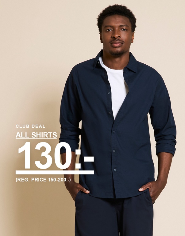 Man i mörkbrun skjorta över vit topp och blå denimshorts. CLUB DEAL. ALL SHIRTS 130:- (REG. PRICE 150-200:-)