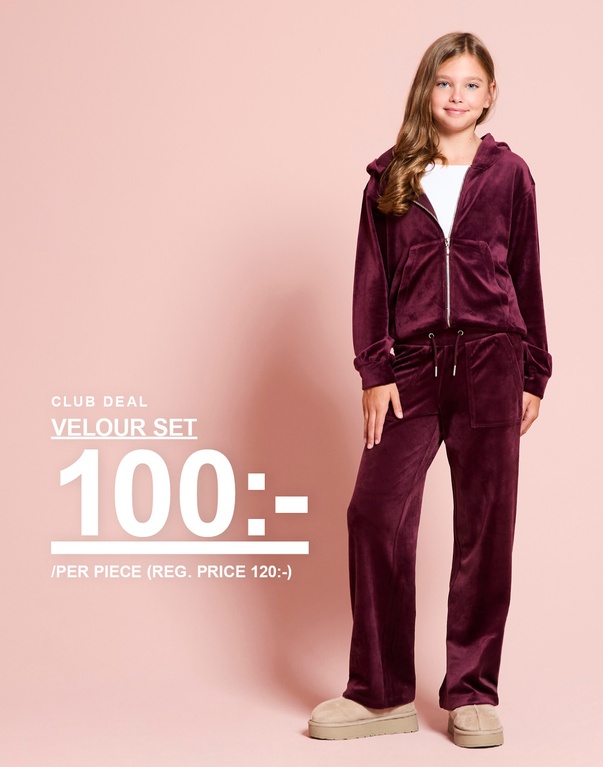 En tjej bär ett vinrött velourset med huvtröja och byxor. CLUB DEAL – VELOUR SET 100:- / PER PIECE (REG. PRICE 120:-).