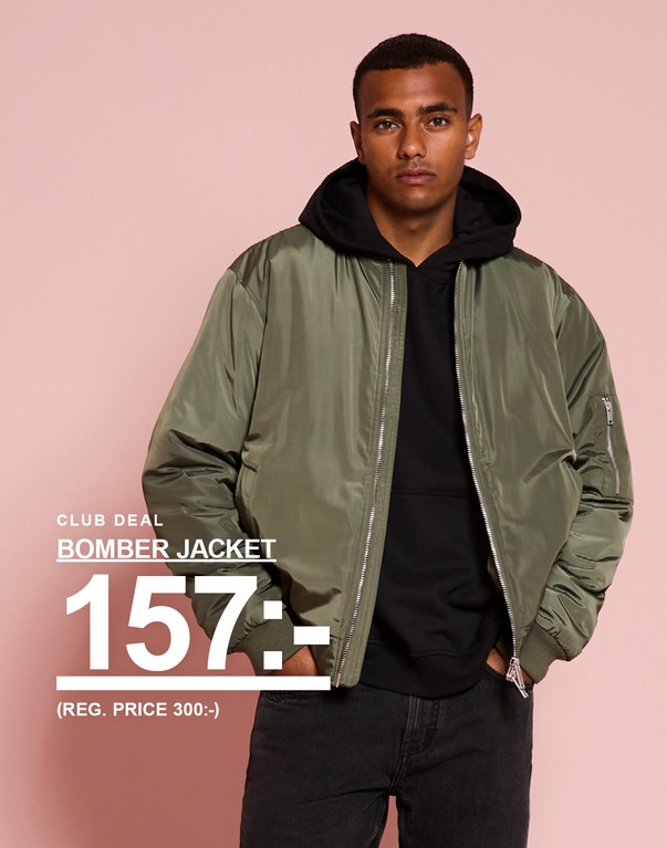 En kille i grön bomberjacka över svart hoodie. Kampanjtext: “CLUB DEAL BOMBER JACKET 157:- (REG. PRICE 300:-)”.