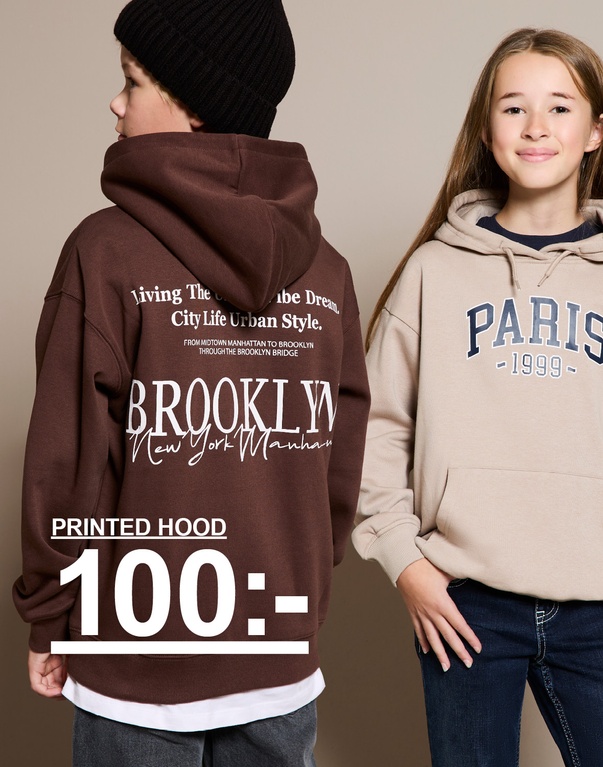 Flicka i beige huvtröja med texten "Paris 1999" och pojke i brun huvtröja med texten "Brooklyn". Text: "Autumn 2025. Printed hood 100:-".
