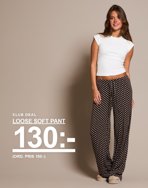 Kvinna i vit topp och bruna byxor med vita prickar. Kampanjtext: "CLUB DEAL: LOOSE SOFT PANT, 130:-".