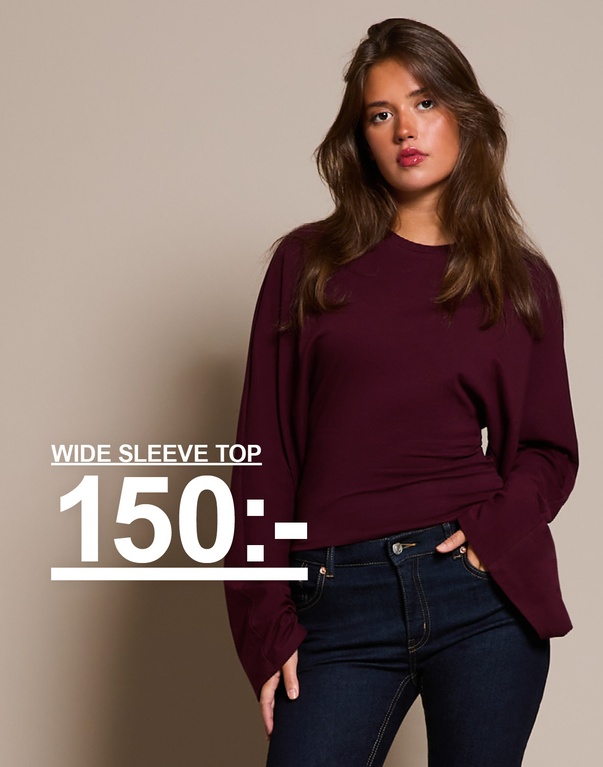 "Tjej i burgundy topp med vida ärmar och mörkblå jeans. Kampanjtext: 'WIDE SLEEVE TOP, 150:-'."