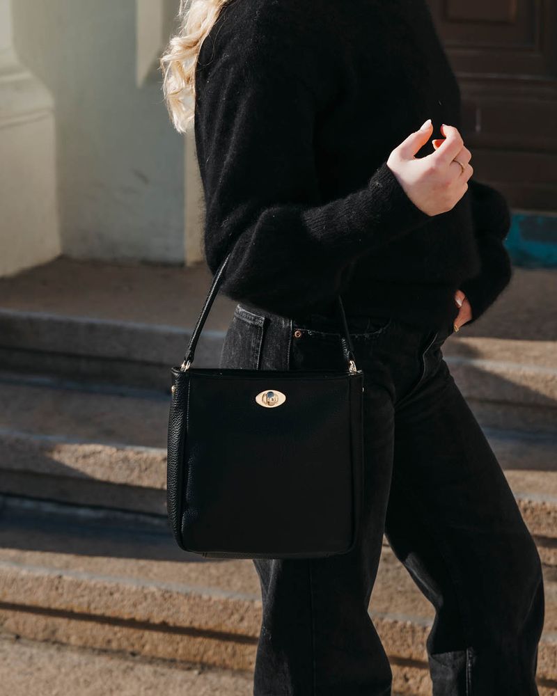 Svart crossbodyväska från Lycke Oslo med guldfärgad detalj, buren diagonalt av en person i svart outfit.