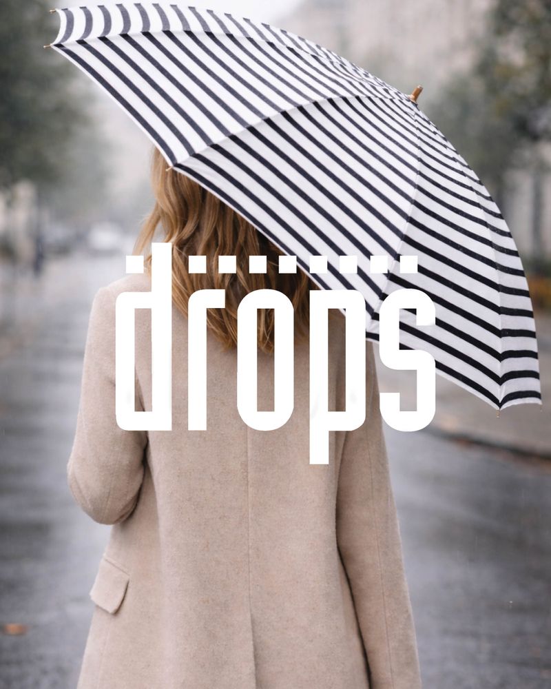 Person som håller ett randigt paraply utomhus i regnigt väder. drops logo