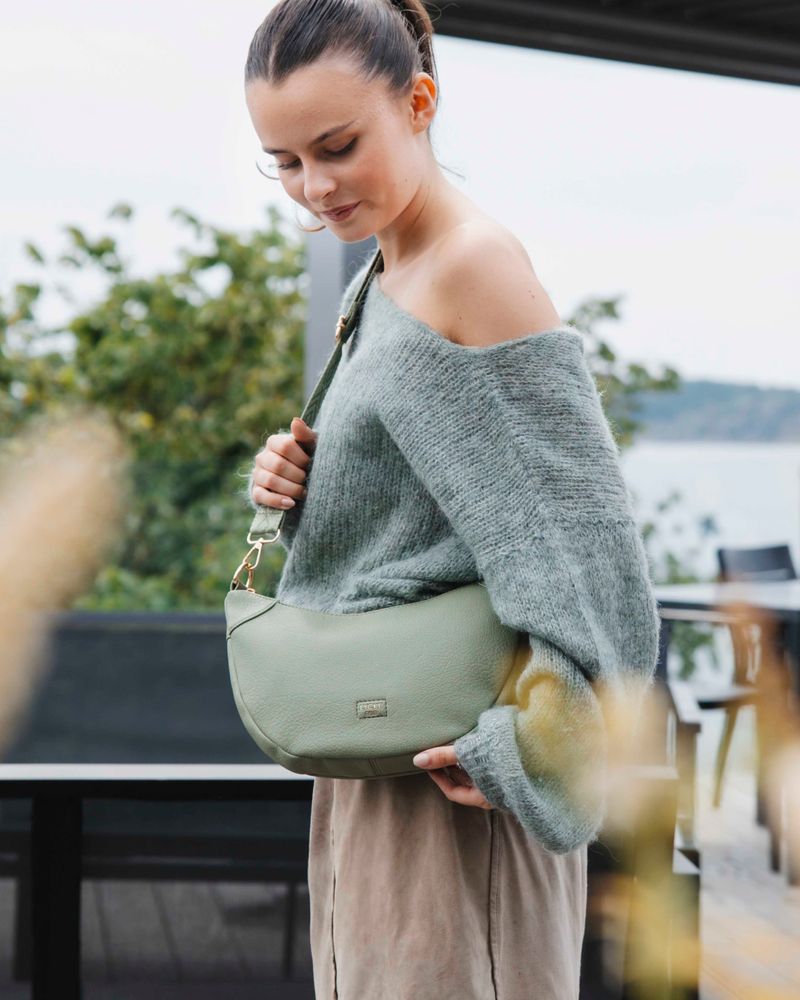Grön crossbody väska från Lycke Oslo. kvinna med grå stickad tröja och beige kjol