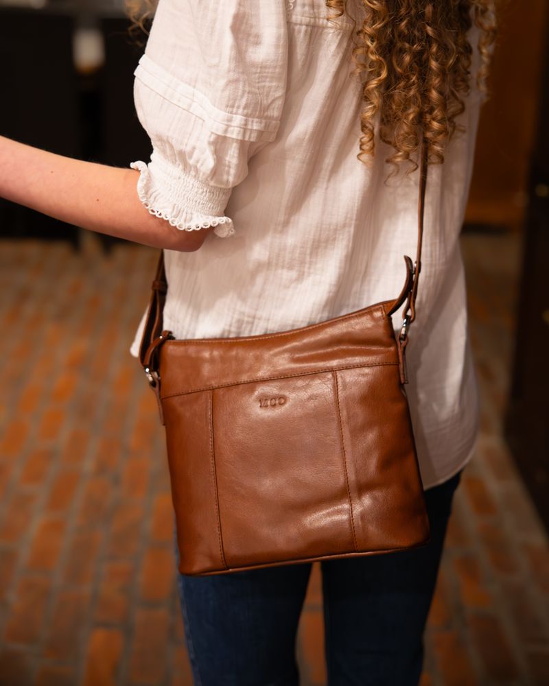 bridge färgad crossover i skinn hänger över axel på kvinna i vit blus och jeans