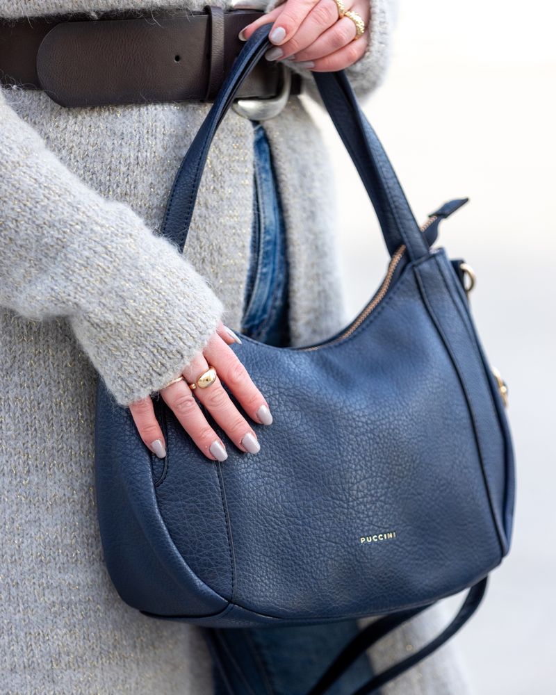 blå handväska från Puccinbi i konstläder, buren av en person i ljus stickad tröja.