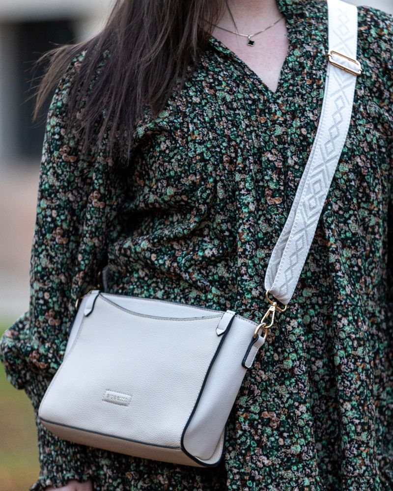 Beige crossbodyväska från Puccini i slätt konstläder, buren över axeln av en person i blommig klänning