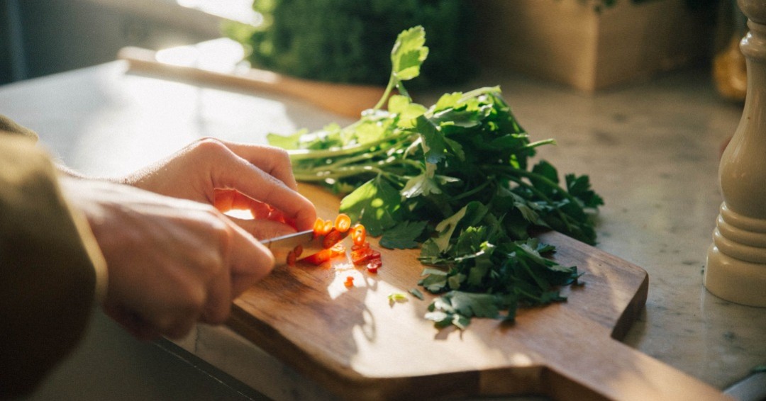 Händer som hackar grönsaker på skärbräda
