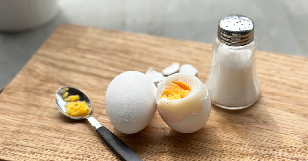 Ett kokt, halvt skalat ägg med sked och saltströare bredvid