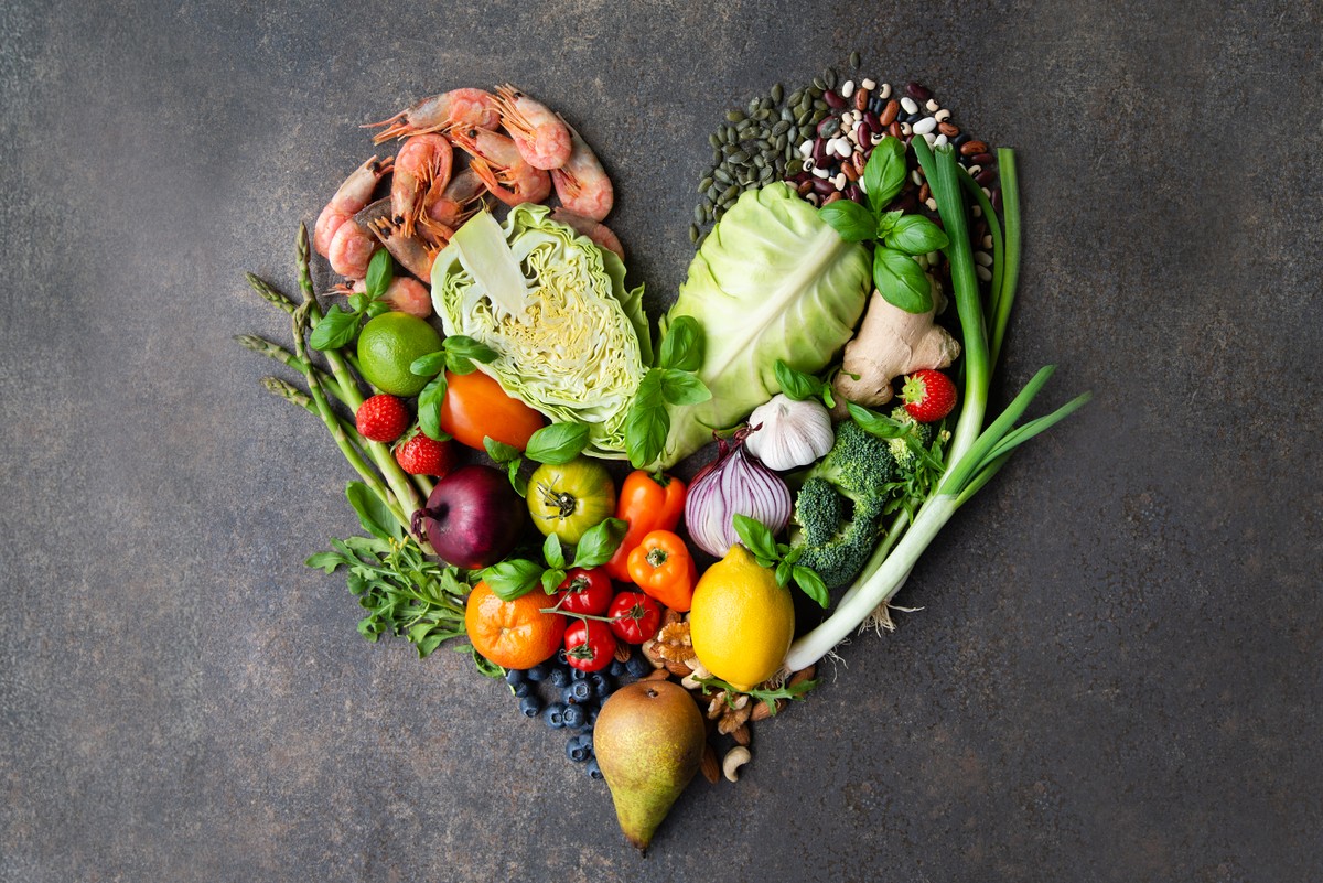 Olika råvaror som frukt, grönsaker och skaldjur ligger i formation av ett hjärta mot grå bakgrund