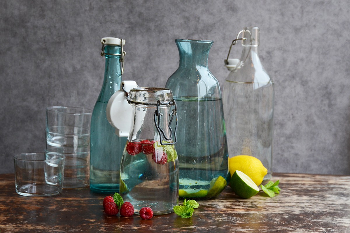 Dricksglas och karaffer i glas med vatten, bär och citrusfrukter i
