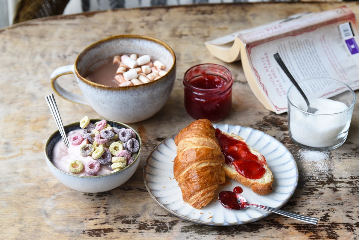 En croissant med sylt, en skål med yoghurt och sockriga flingor samt en kopp varm choklad med marshmallows.