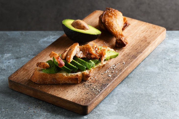 En delad croissant med avokado och kyckling på ligger på en skärbräda i trä