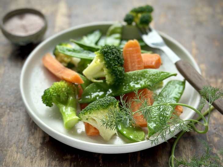 En tallrik med ångkokta grönsaker som broccoli, morötter och ärtskott