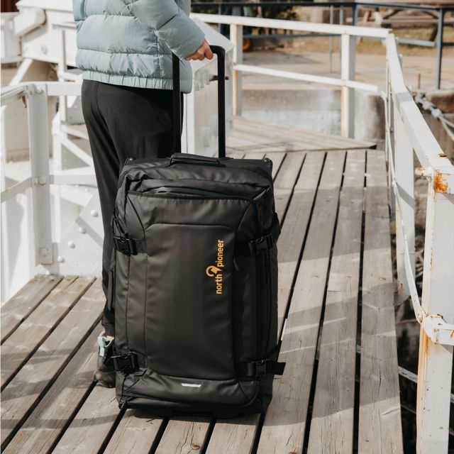 Myk reisebag med hjul, trukket av person på brygge ved vann.