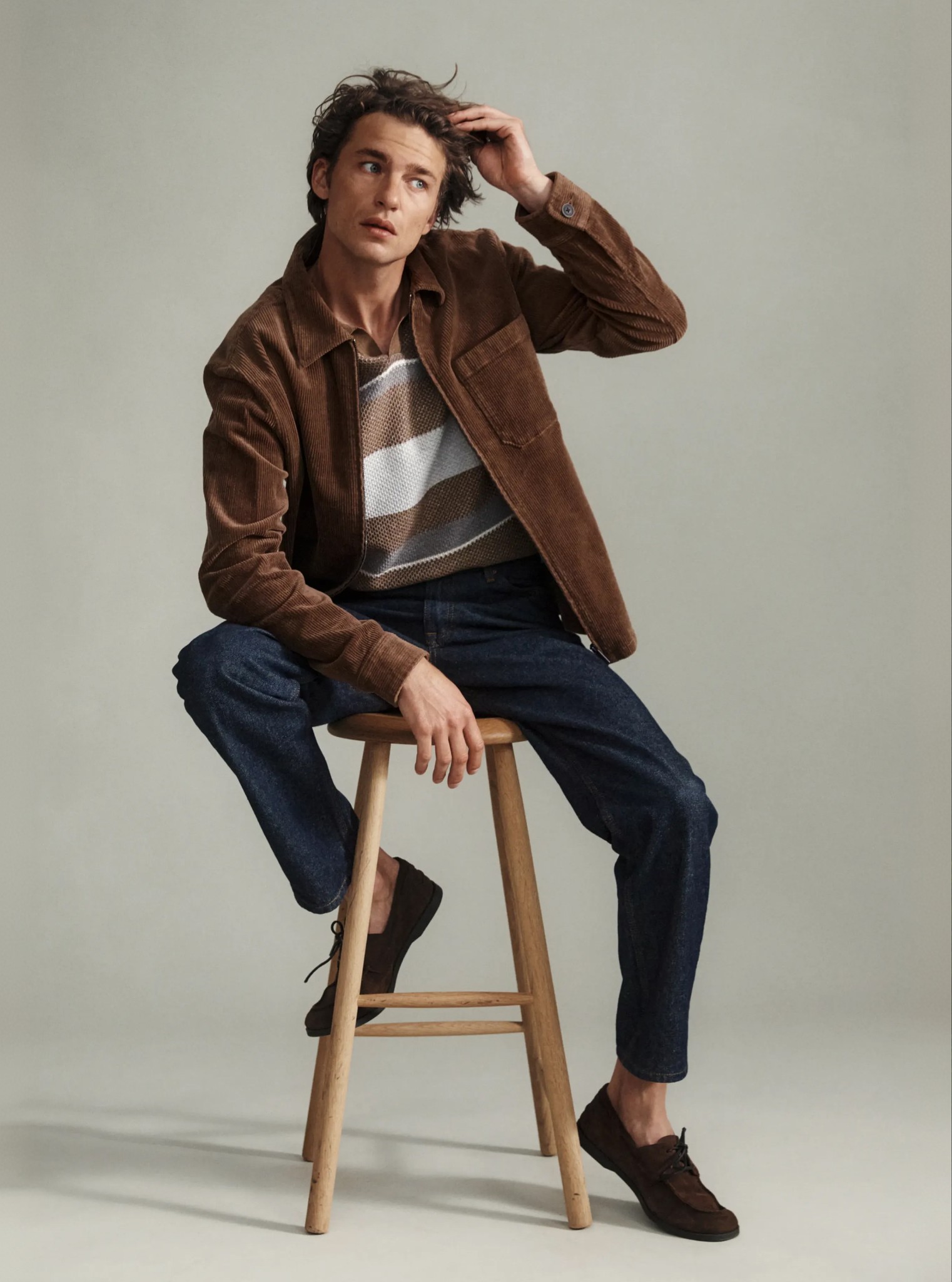 Mand sidder på en stol iført en brun overshirt og marineblå bukser fra MQ Marqet.