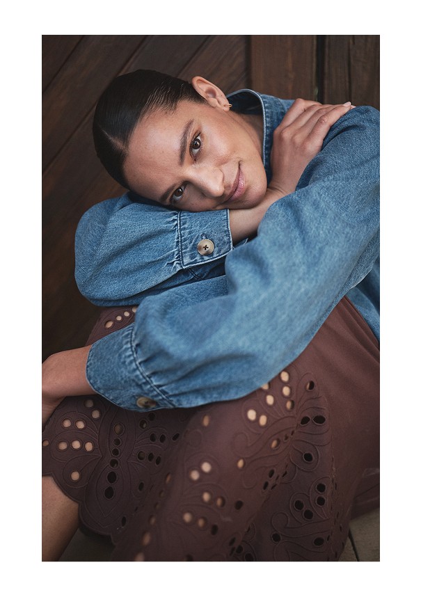 Kuva tytöstä, joka istuu ja jolla on päällään farkkutakki ja ruskea hame MQ:lta.