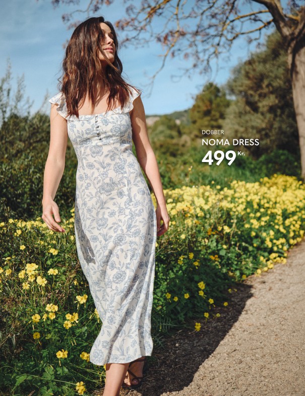 Dame i hvid sommerkjole med lyseblåt blomstermønster. I baggrunden mange gule blomster.