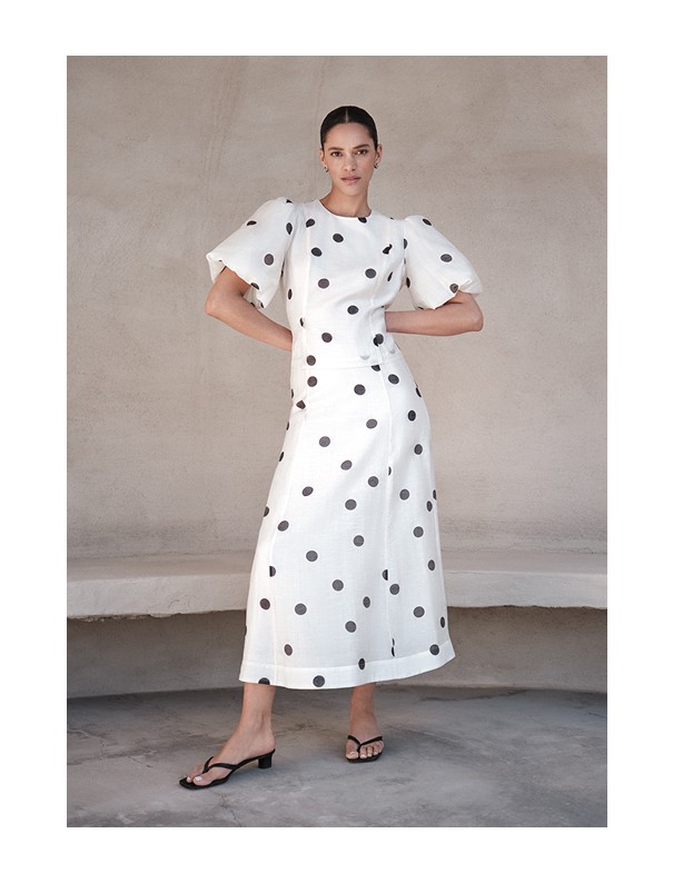 Tyttö, jolla on päällään valkoinen setti, jossa on puffihihoinen pusero ja hame mustilla pilkuilla MQ Marqet:lta.