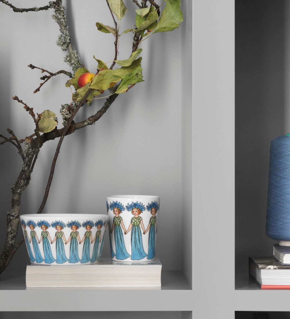 En bokhylla med en skål och mugg med motiv av Elsa Beskow