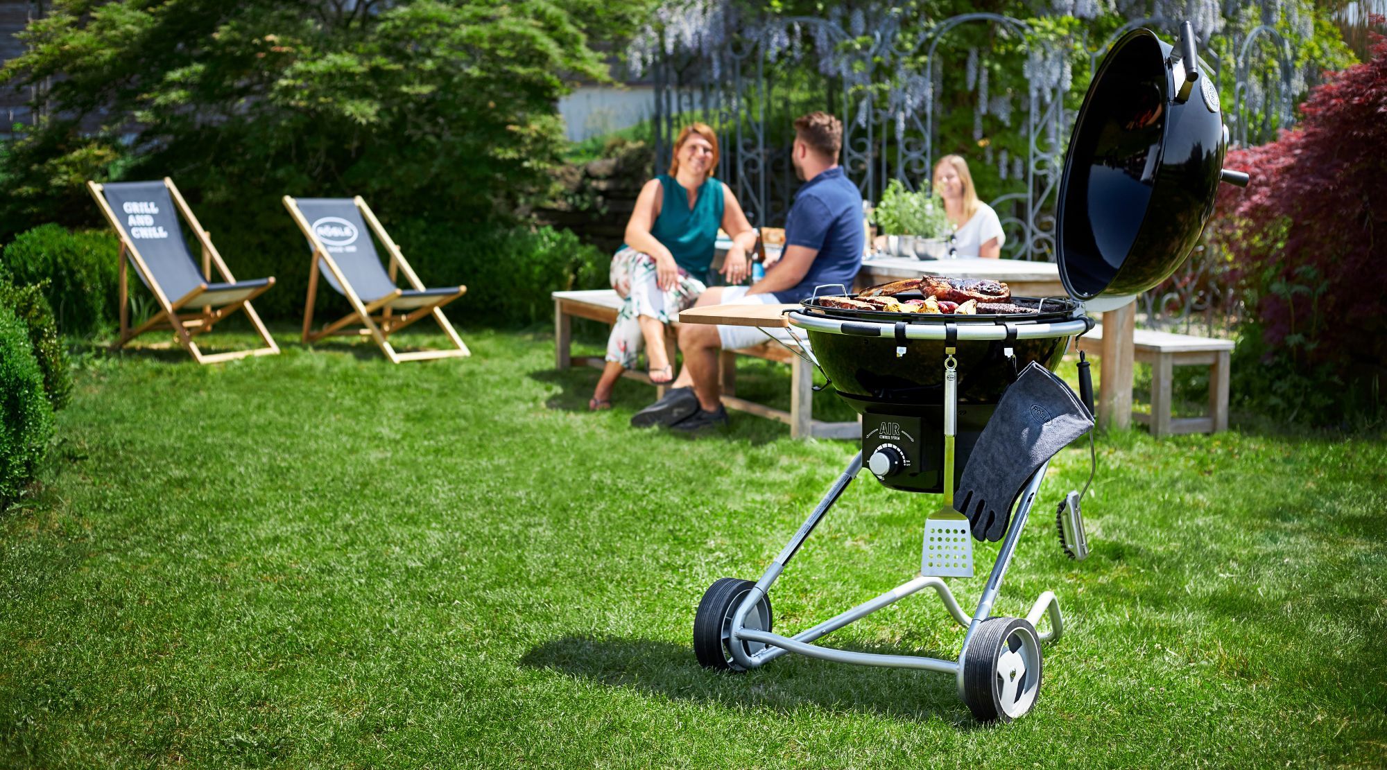 Ett svart kolgrill ståendes på en grön gräsmatta med människor i bakgrunden.