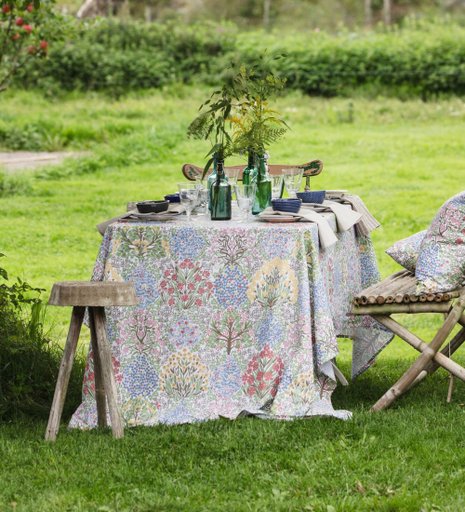 Ett fint dukat bord med en blommig duk i en grön trädgård med trämöbler
